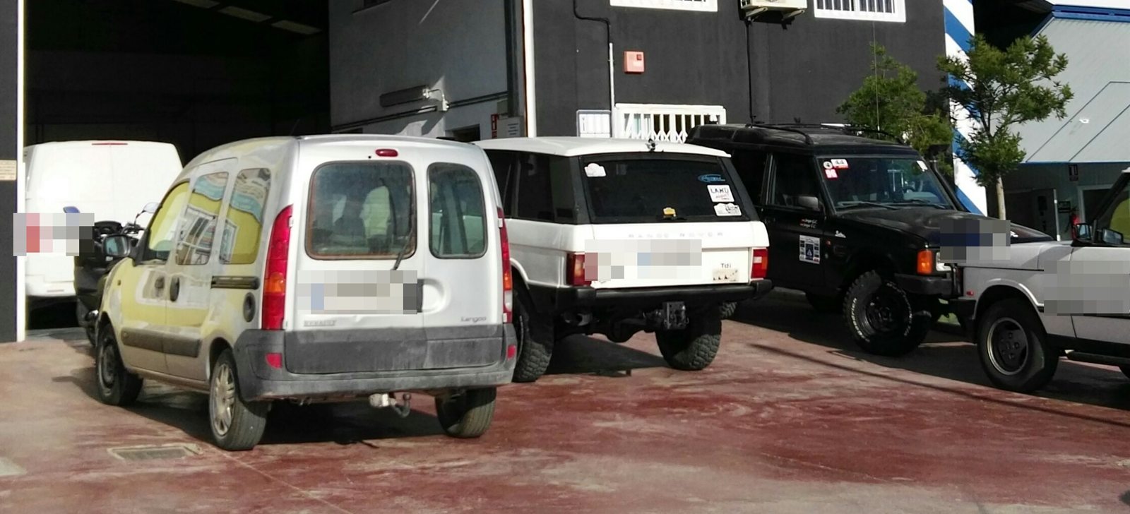 Fila de vehículos aparcados en el patio del taller, entre ellos varios todoterreno clásicos