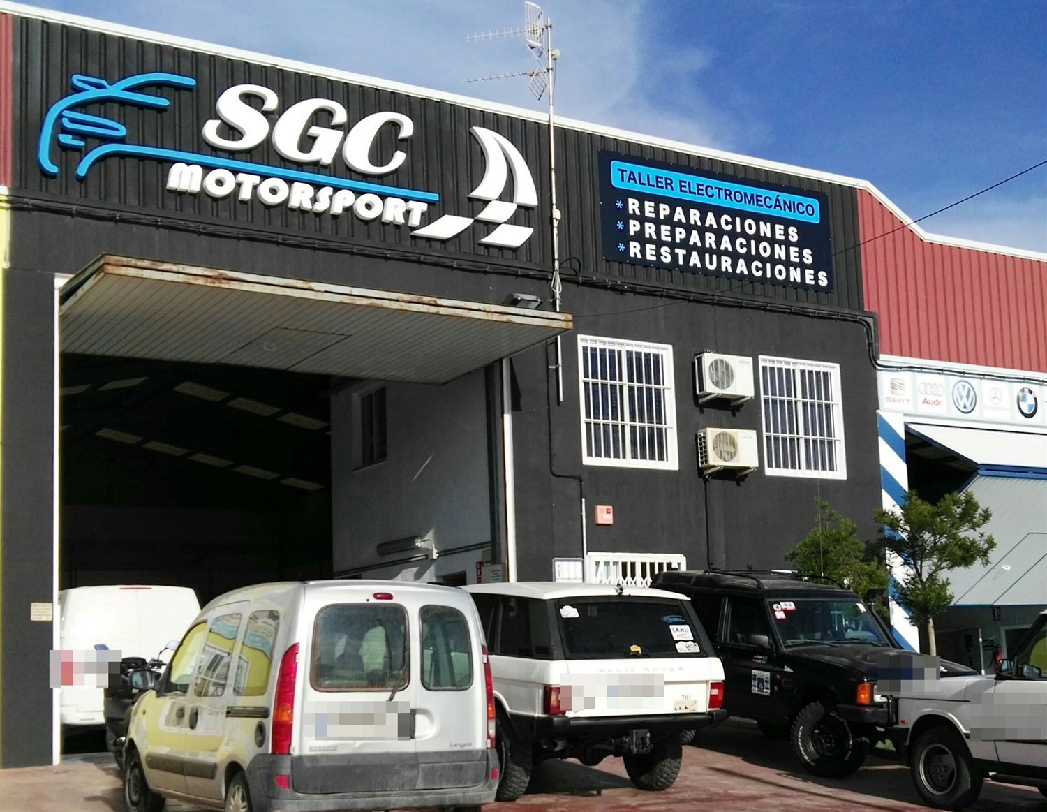 Nave de SGC Motorsport vista desde la calle, con el rótulo sobre la chapa negra y el portón abierto